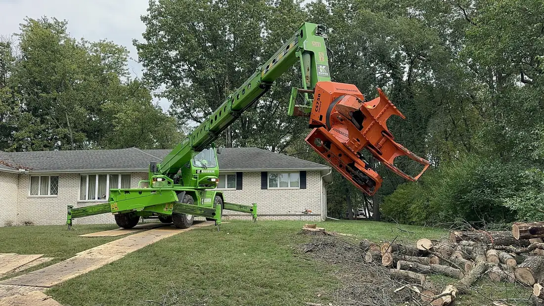 KVM crane with grapple saw working beside a home, set up on ground mats